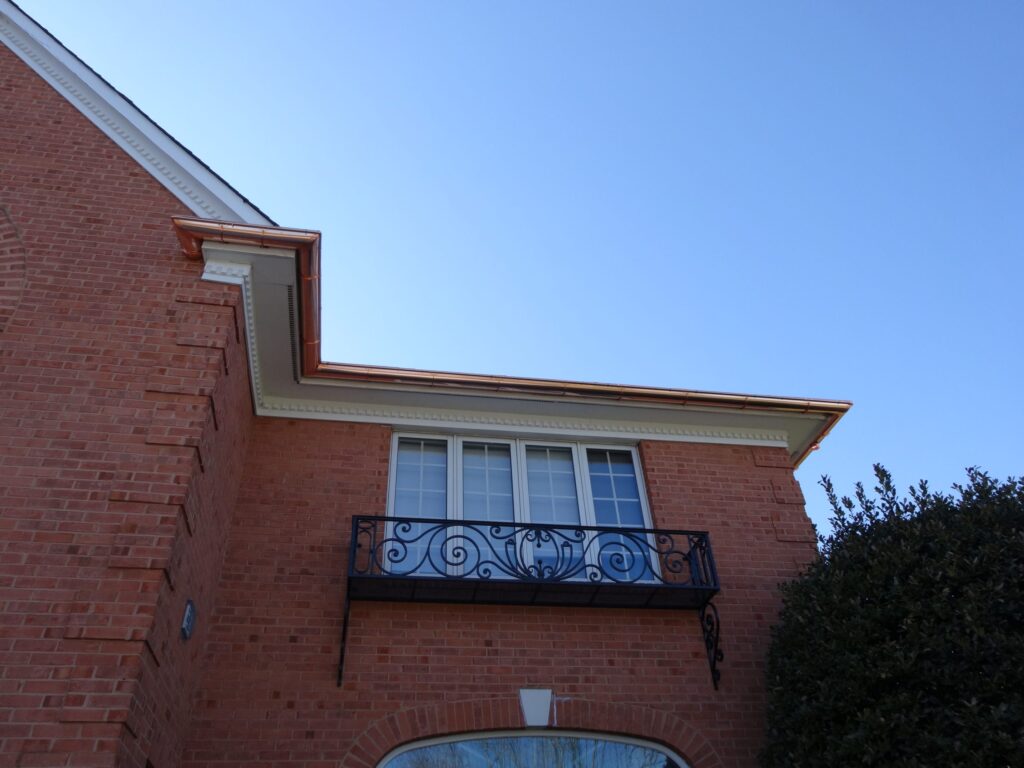 Copper downspout running down brick beside a balcony